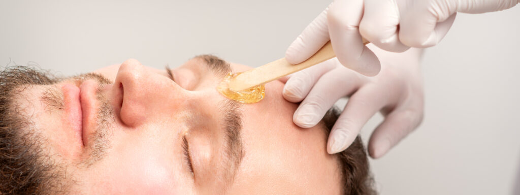 Beautician applying wax paste between eyebrows during the procedure of waxing in the beauty salon.